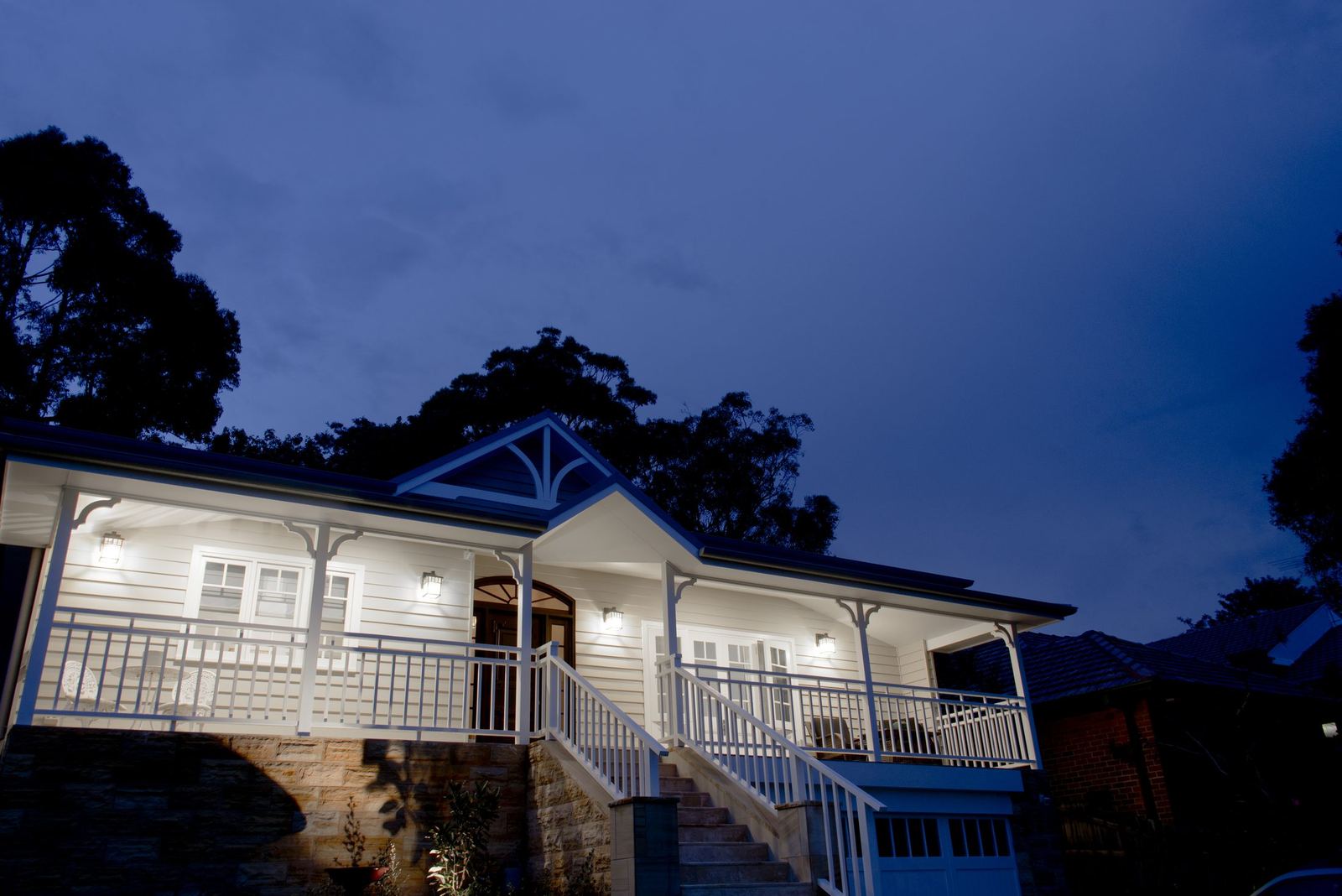 Balgowlah, dusk view of the weatherboard home with a lit veranda and garden, built by HP Constructions with Scope Architects