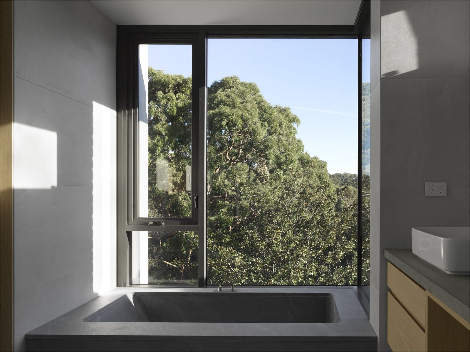 Castle Cove, bathroom with stone bath beneath full-height window overlooking trees, built by HP Constructions with Dieppe Design