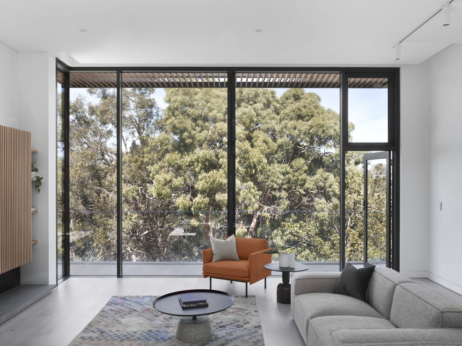 Castle Cove, living room with full-height glazing to trees, tan armchair and grey sofa, built by HP Constructions with Dieppe Design