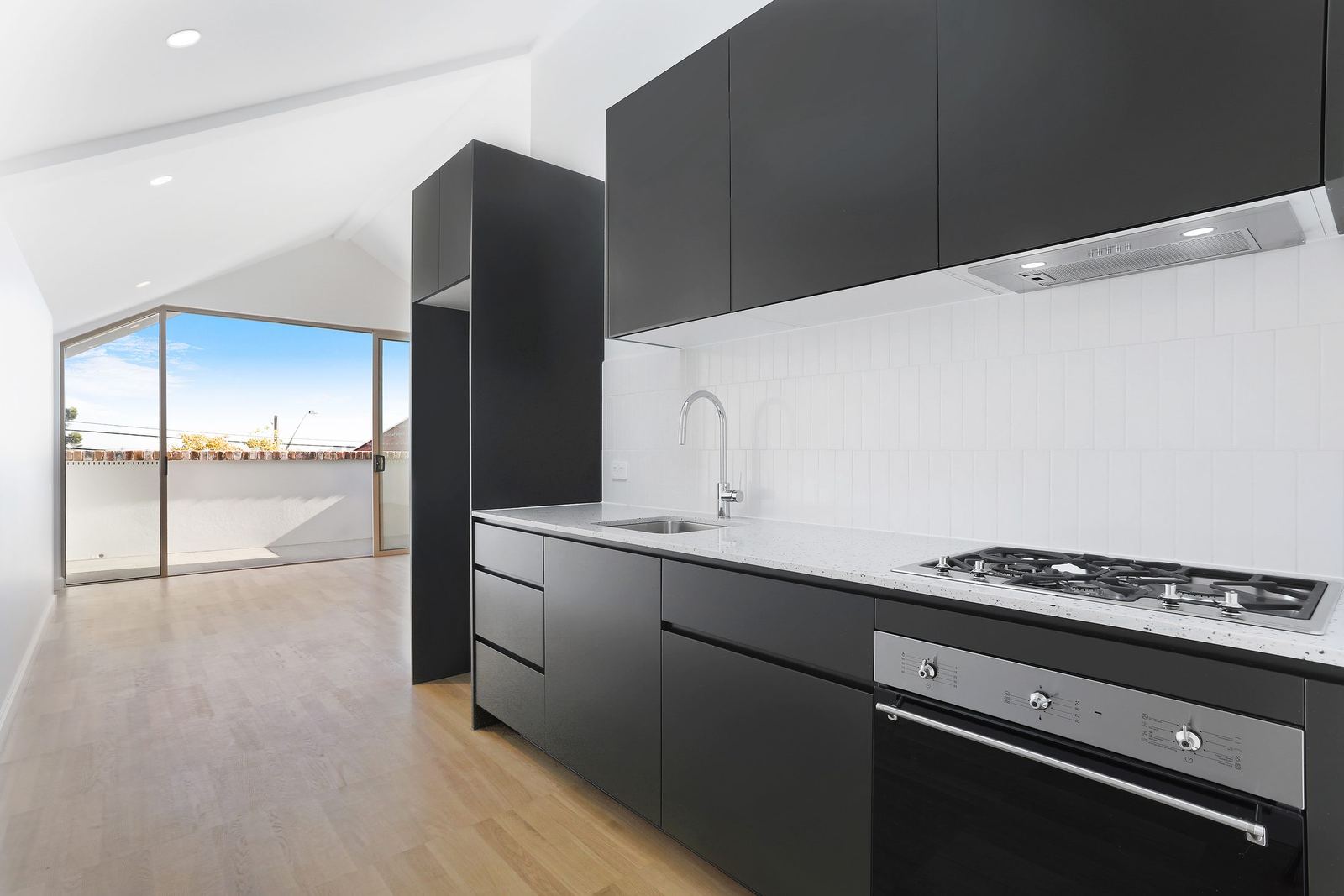 Queens Park Apartments, black kitchen cabinetry with gas cooktop and white splashback, built by HP Constructions with Ignite Architects