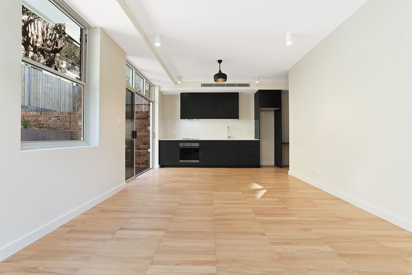 Queens Park Apartments, open living space with black kitchen and exposed brick wall, built by HP Constructions with Ignite Architects