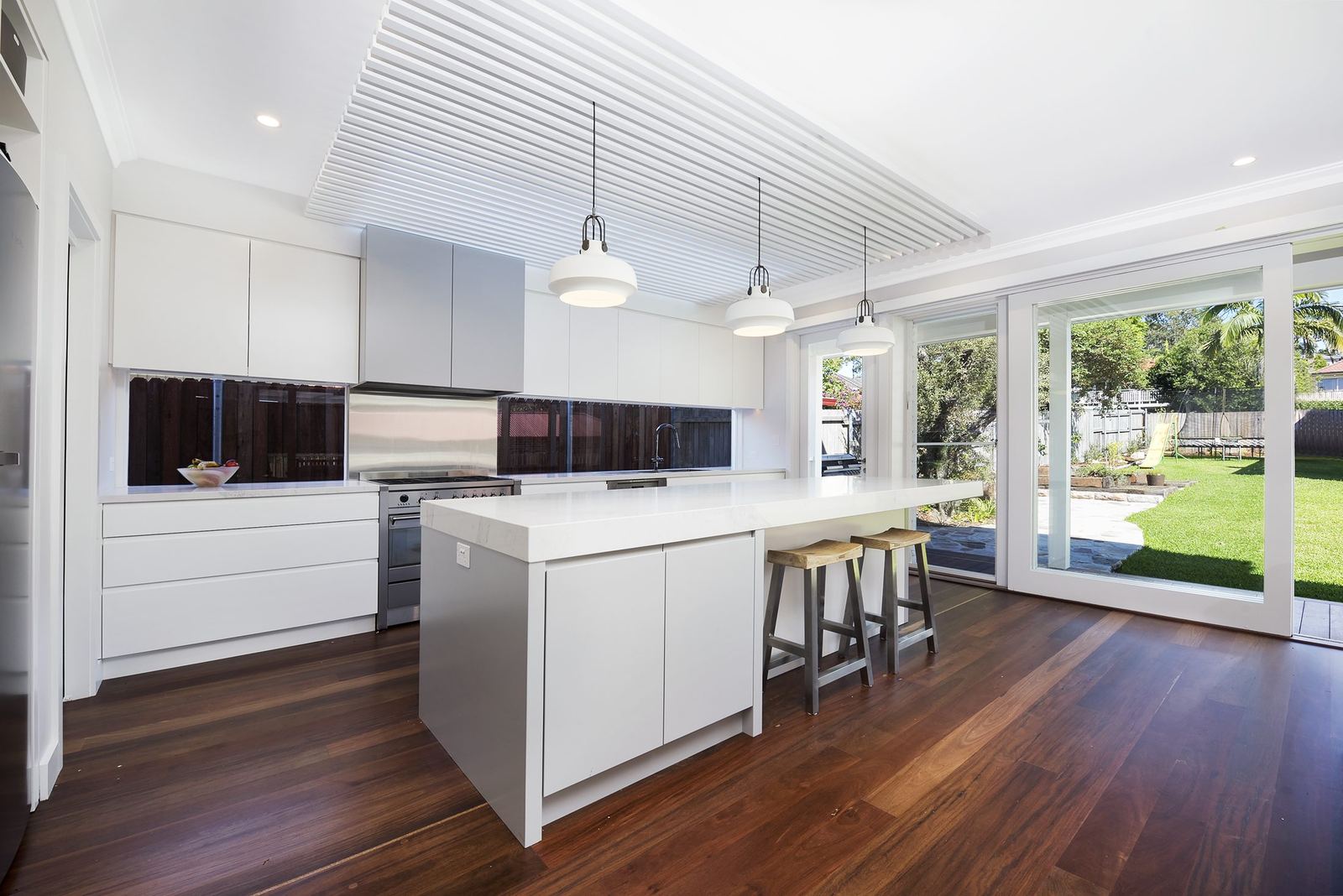 Seaforth, white kitchen island with pendant lights and sliding doors to garden, built by HP Constructions with Playoust Churcher